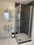 Badezimmer mit weiß gefliesten Wänden, Waschbecken, Spiegel und einer Duschkabine mit grauen Wänden.