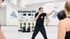 Ein Boxtrainer im schwarzen T-Shirt zeigt einer Frau in einem hellen Boxstudio eine Schlagtechnik.