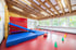 Heller Turnraum für Kinder mit Holzdecke, blauen Weichbodenmatten, einer Rutsche und bunten Pylonen auf rotem Boden.
