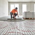 Handwerker glättet frischen Estrich über einer verlegten Fußbodenheizung mit Noppenplatten in einem Rohbau.