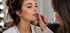 Swetlana Ilicow, Hair & Make-up-Artistin aus Osnabrück, trägt mit einem Lippenkonturenstift Make-up auf die Lippen einer jungen Frau mit hochgesteckten Haaren auf.