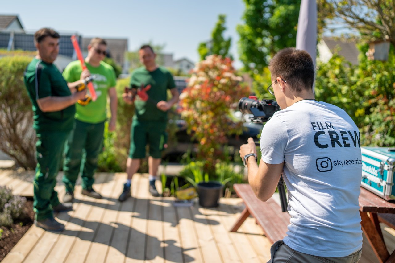 Kameramann filmt drei Mitarbeiter eines Garten- und Landschaftsbaubetriebs bei der Arbeit