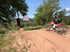 Ein Motocross-Fahrer auf einem orangefarbenen Motorrad fährt auf einer Sandpiste; ein Mann hält ein weißes Brett.