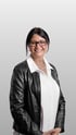 Birgit Birk, Business-Porträt einer Frau mit schwarzer Brille, dunkler Lederjacke und weißer Bluse vor neutralem Hintergrund.