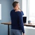 A man stands at a wooden standing desk and rubs his shoulder while looking out a window.