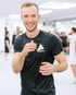 Max - Boxtrainer BACKYARD Wien - Trainer lächelt in Boxing Stance in die Kamera während im Hintergrund das Boxtraining stattfindet