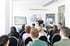 Ein Dozent hält einen Vortrag vor sitzenden Studenten in einem hellen Konferenzraum.