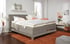 Modernes Boxspringbett in Grau mit verstellbarem Kopfteil und weißer Bettwäsche, auf rustikalem Teppich.