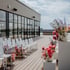 Bestuhlte Dachterrasse für eine Hochzeit mit weißen Stühlen, bunten Blumengestecken und moderner Glasfront.