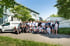 Gruppe von 29 Personen, überwiegend Männer, vor einem Gebäude mit zwei weißen Topwerker Lieferwagen.