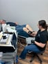 Man lies on a medical bed while a woman in black gloves performs shockwave therapy on his legs.