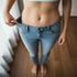 Frau zeigt ihren flachen Bauch und lockere Jeans, die von erfolgreichem Gewichtsverlust zeugen.