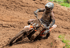 Schlammbedeckter Motocross-Fahrer mit Startnummer 713 fährt in einer steilen Kurve auf einer erdigen Rennstrecke.