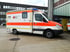 Rettungswagen des Deutschen Roten Kreuzes mit orangefarbenen Streifen und Blaulicht vor einem Gebäude.