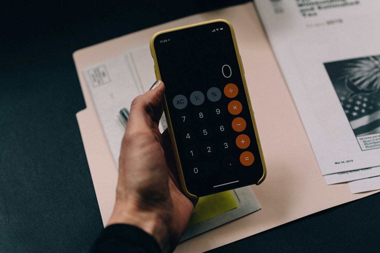 Hand hält ein Smartphone mit Taschenrechner über einem Papierordner