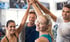 Vier lächelnde Personen im Fitnessstudio, die die Hände in die Mitte heben.