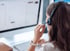 Frau mit Headset am Computerbildschirm, ihre Hand hält das Mikrofon.
