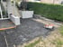 Baustelle für eine Terrasse mit vorbereitetem Untergrund, Steinschneider, Treppenstufen und einer grünen Hecke im Garten.