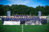 Eine Gruppe von Kindern und Erwachsenen posiert auf einem Fußballfeld vor einem Wald mit Bannern der Buffon Football Academy.