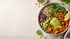 Eine Buddha-Schale mit Kichererbsen, Erbsen, Mais, Avocado, Salat, Tomatenpaste, Leinsamen, einem Holzlöffel und Limettenspalten.