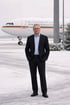 Stephan in schwarzem Anzug und Brille steht vor einem "Bundesrepublik"-Flugzeug im Schnee.