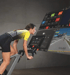 Frau trainiert auf einem Indoor-Bike vor einem großen Monitor mit virtueller Strecke und Fitness-Datenanzeige.