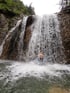 Person mit Helm steht unter einem großen Wasserfall.