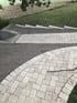 Neu gepflasterter Gartenweg aus hellen Steinplatten im Fischgrätmuster neben einer unbefestigten Erdfläche.