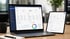 Laptop und Tablet zeigen eine Finanzanalyse-Software mit Diagrammen und Zahlen auf einem Holztisch.