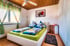 Schlafzimmer mit weißem Doppelbett, grünem Bettzeug, Deckenventilator und Fenster mit gestreiften Vorhängen.