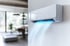 Weiße Klimaanlage an der Wand, die kühle, blaue Luft in einen modernen Wohnraum bläst.
