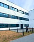 Modernes Backsteingebäude mit mehreren Stockwerken und Fenstern, umgeben von Grünflächen und einem gepflasterten Weg.