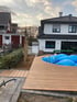 Ein Garten mit Holzterrasse, eingelassenem Pool mit blauer Abdeckung und einem modernen Einfamilienhaus im Hintergrund.