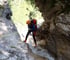 Person beim Canyoning, die sich mit Seil und Helm in einen Wasserfall abseilt.