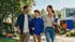 Smiling parents and a teenage son walking together outside, carrying school supplies near a modern building.