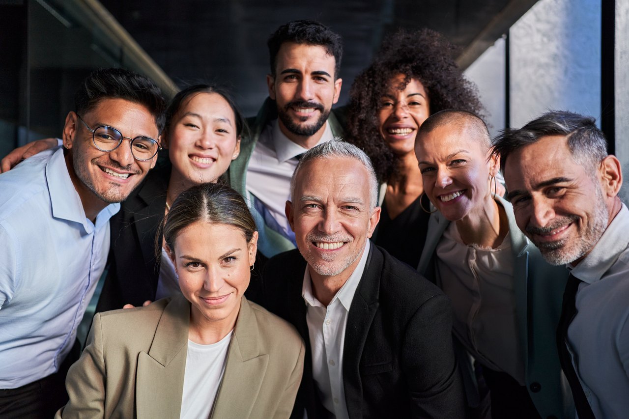 Acht lächelnde, vielfältige Geschäftsleute blicken in die Kamera – ein Team mit klarer gemeinsamer Haltung.