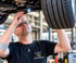 KFZ-Mechaniker vom Autohaus Wetterauer inspiziert den Unterboden eines Autos auf einer Hebebühne mit einer Taschenlampe.