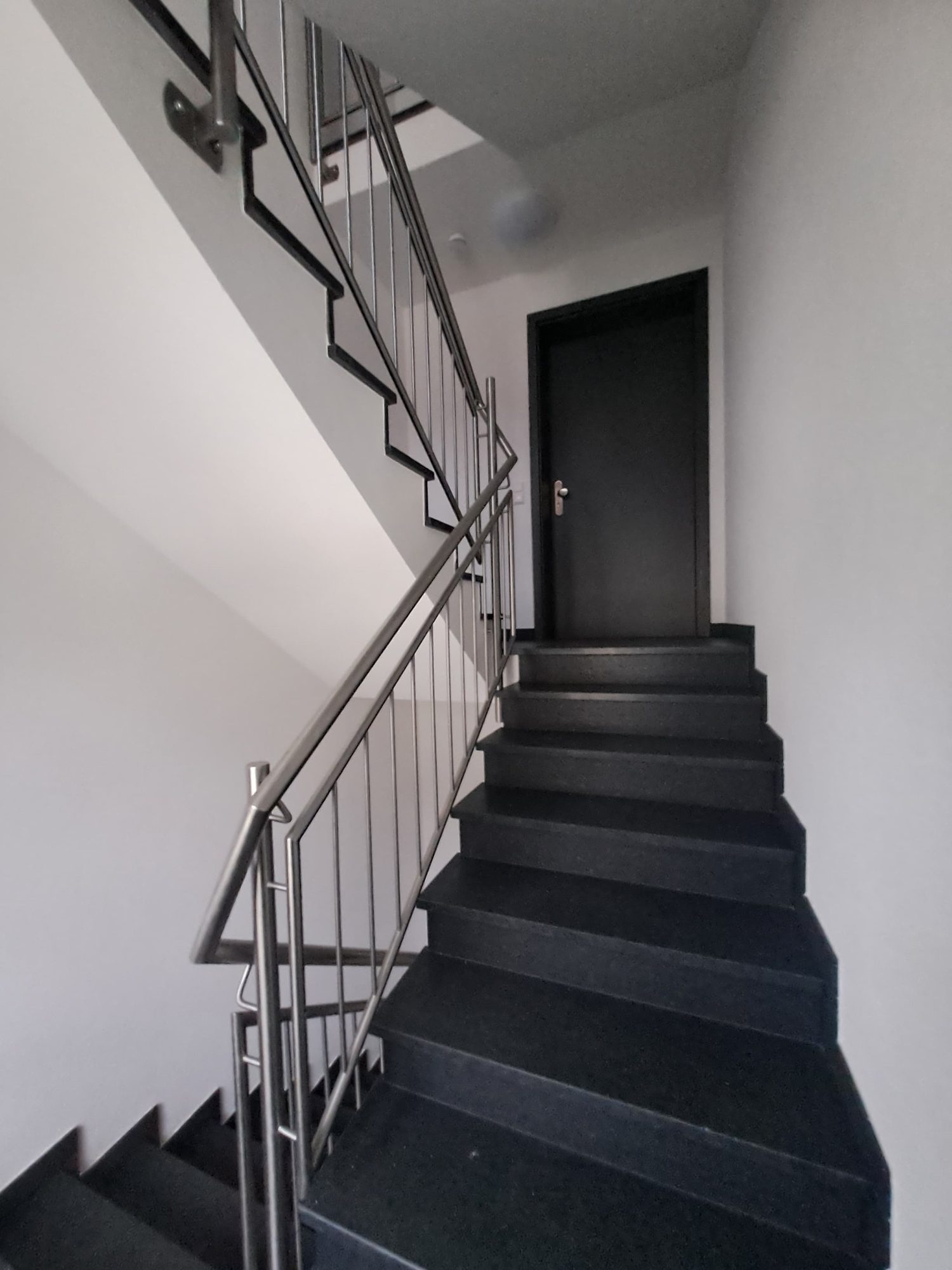 Treppenhaus mit Edelstahlgeländer und dunklen Stufen