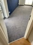 Ein Raum mit dunkelblau gestrichener Wand und grauem Teppichboden, Holzboden im Türrahmen.
