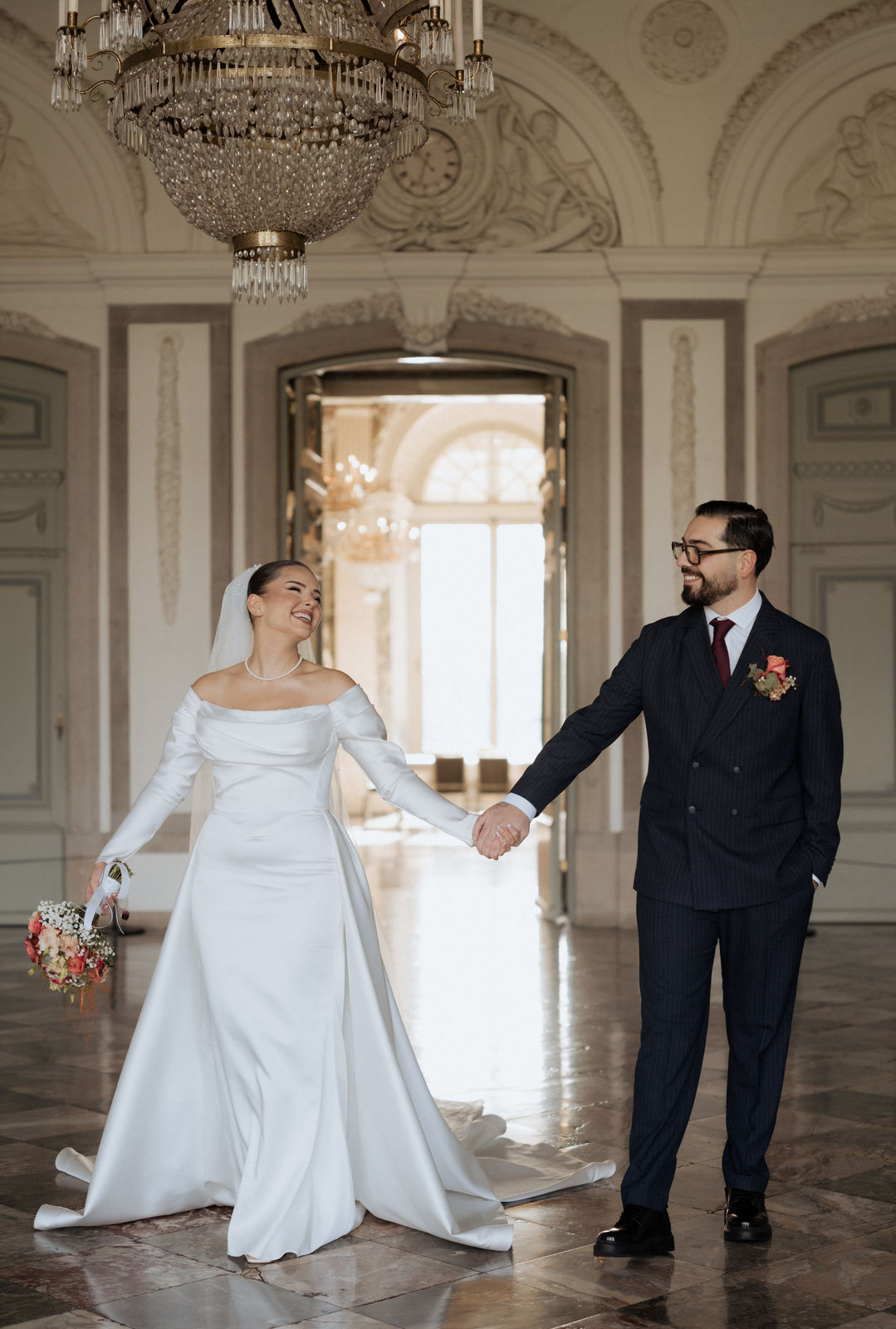 Brautpaar Hand in Hand vor der hohen Fenstertür im Schloss Benrath in Düsseldorf.