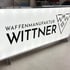 Leuchttransparent mit dem Schriftzug "WAFFENMANUFAKTUR WITTNER" und einem Logo in Weiß und Schwarz.