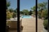 Moderner Garten mit Pool, Holzterrasse, Loungemöbeln und grüner Bepflanzung durch ein Fenster betrachtet.