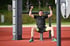 Mann trainiert Oberkörper an einem Outdoor-Fitnessgerät auf einer roten Sportfläche.