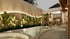A modern outdoor space with a curved swimming pool, lush plants, and warm accent lighting along a wall and the building.