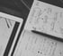 Schwarz-Weiß-Foto: Skizzen und Notizen in einem Notizbuch neben einem Tablet – Strategieberatung und Online-Marketing für Handwerksbetriebe zur Neukunden- und Mitarbeitergewinnung.