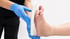 Orthopädie-Fachkraft mit blauen Handschuhen passt eine weiße orthopädische Einlegesohle an einen nackten Fuß an.