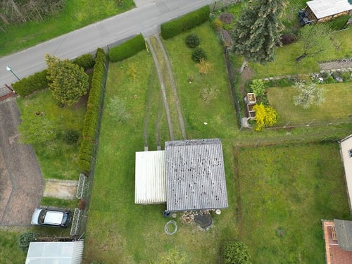 Luftaufnahme eines kleinen Hauses mit Garten, Zufahrt und angrenzender Straße.