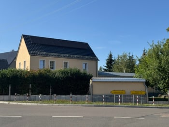 Straßenansicht des Hauses mit Solaranlage auf dem Dach hinter einem Zaun