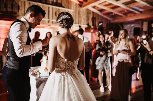 Brautpaar schneidet die Hochzeitstorte vor Gästen im Almhütten-Raum