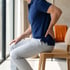 A man in a blue polo shirt sits on a wooden chair while holding his lower back.